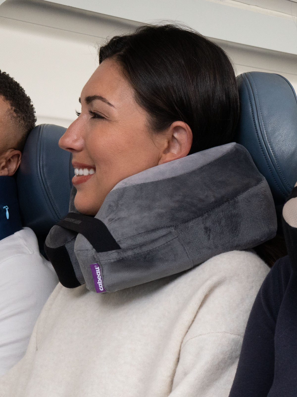 Woman using a black and grey travel neck pillow on an airplane