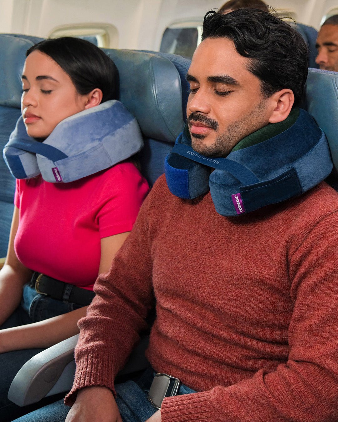 Evolution Earth Deluxe Neck Pillow - Woman wearing Water pillow (light/medium blue) . Man wearing Terra pillow (dark blue/green) on airplane